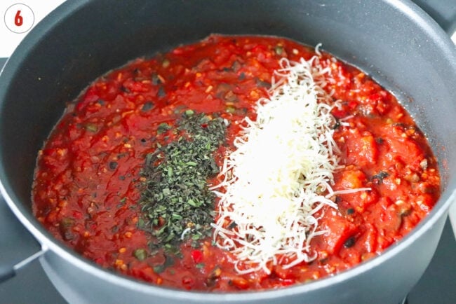 Grated Parmigiano Reggiano cheese and chopped fresh oregano in a pan with spicy tomato sauce.