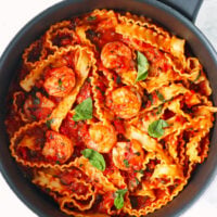 Puttanesca pasta with shrimp garnished with basil leaves in a skillet.