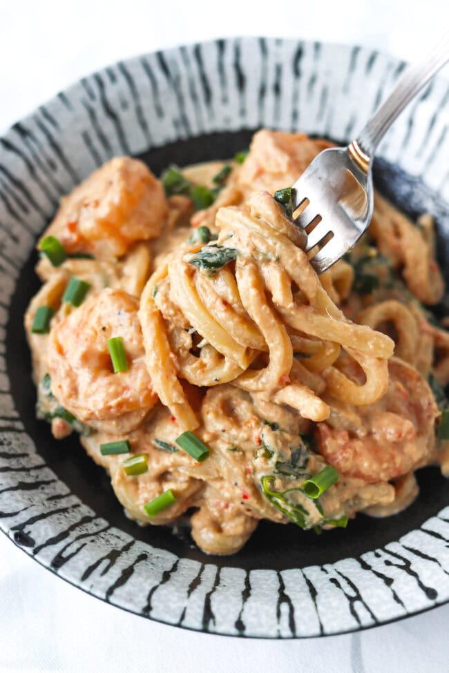 Closeup of fork pulling up a bite of Spicy Tahini Peanut Noodles with shrimp from a plate.