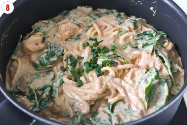 Green onions in pan of silken tofu and tahini sauce udon noodles with spinach and shrimp.