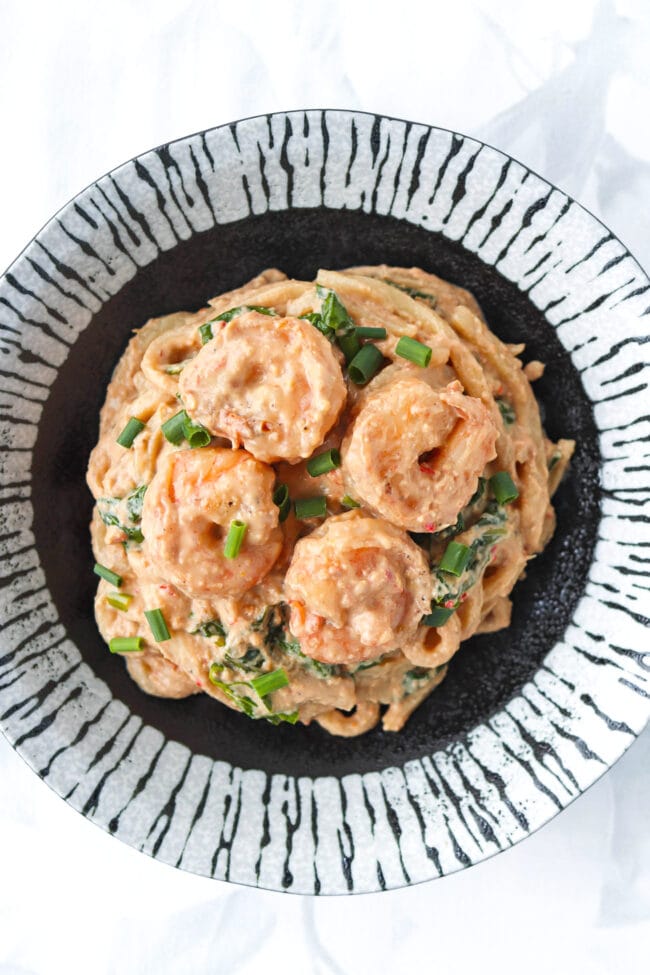 Top view of plate with Spicy Tahini Peanut Udon Noodles with shrimp, spinach and green onions.