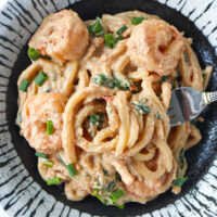 Fork in plate with chili oil tahini peanut butter udon noodles with shrimp, spinach and green onions.