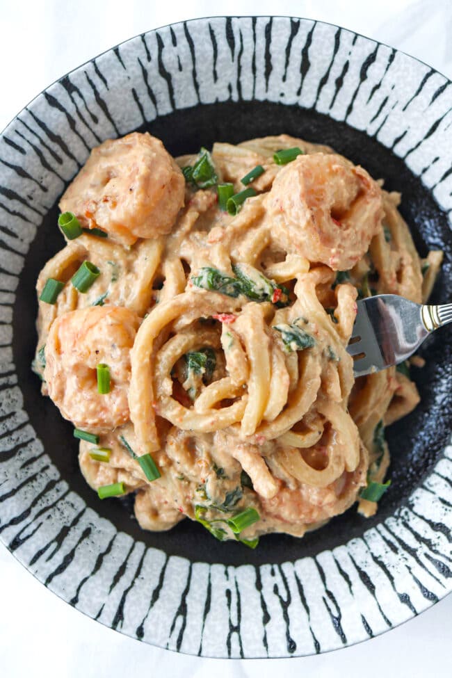 Fork in plate with chili oil tahini peanut butter udon noodles with shrimp, spinach and green onions.
