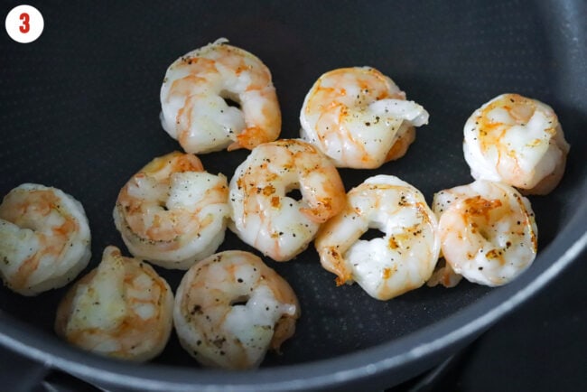 Seared salt and pepper seasoned jumbo shrimp in a pan.