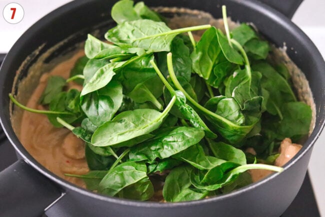 Baby spinach in pan of creamy tahini peanut butter and chili oil udon noodles.