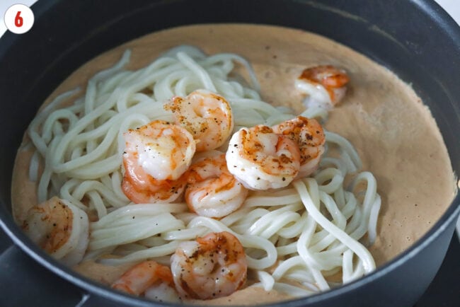 Cooked shrimp and udon noodles in a pan with blended silken tofu, tahini, peanut butter and chili oil sauce.