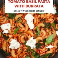 Closeup of skillet with tomato pasta with spinach topped with basil and black pepper seasoned torn burrata. Text overlay "Tomato Basil Pasta with Burrata", "Speedy Weeknight Dinner!" and "That Spicy Chick".