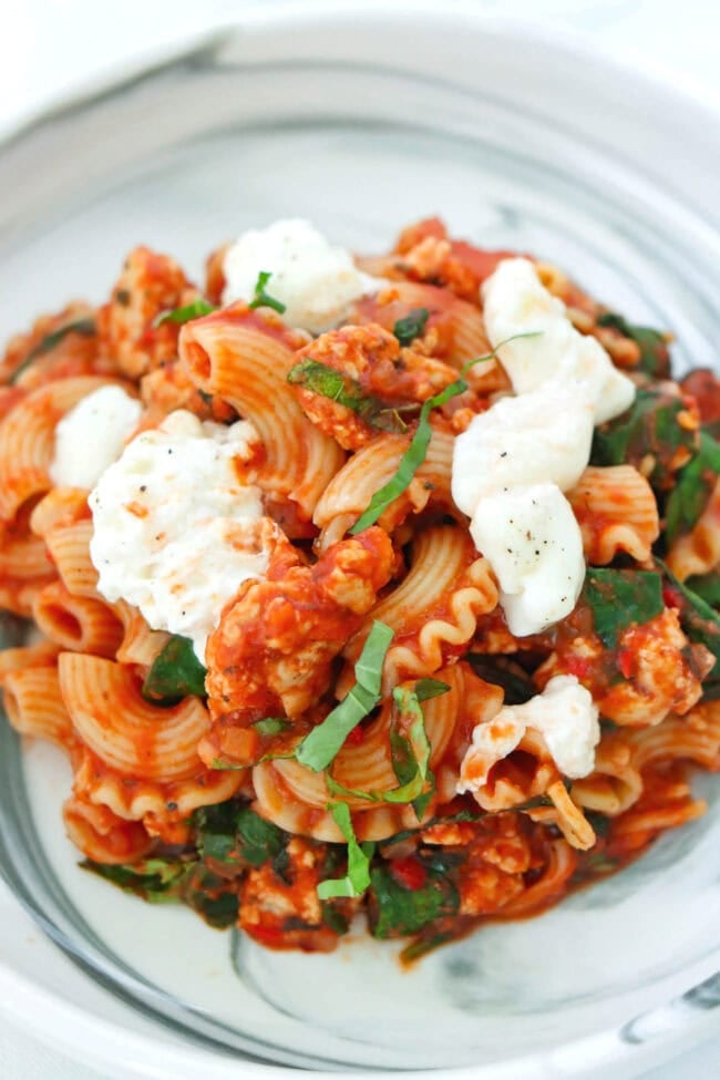 Front view of plate with tomato basil pasta topped with basil and torn burrata that's seasoned with black pepper.