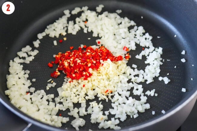 Minced garlic and chilies in pan with sautéed finely chopped yellow onion.