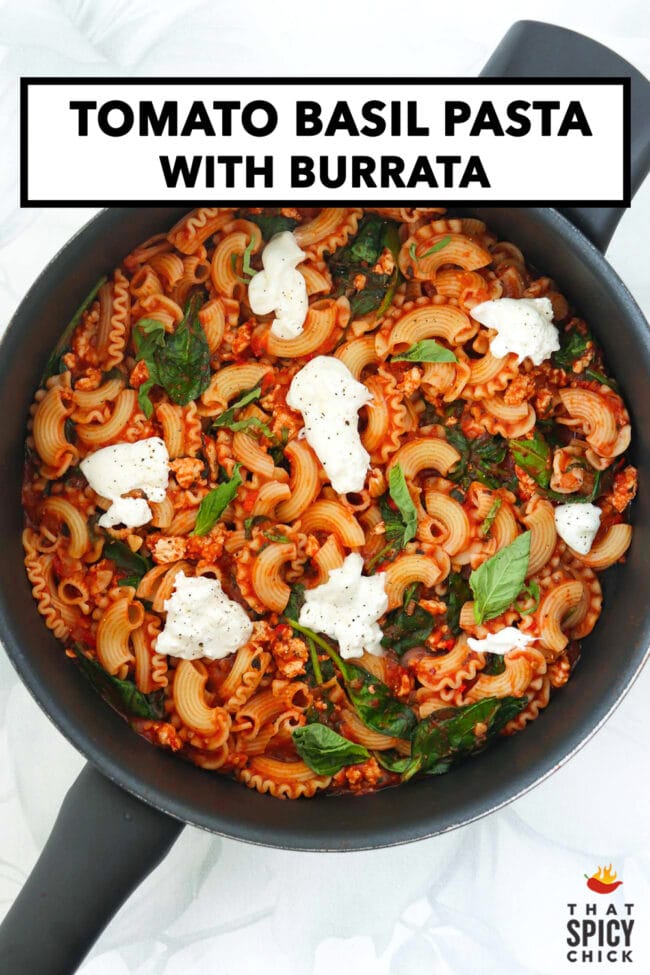 Skillet of tomato pasta with spinach topped with basil and black pepper seasoned torn burrata. Text overlay "Tomato Basil Pasta with Burrata" and "That Spicy Chick".