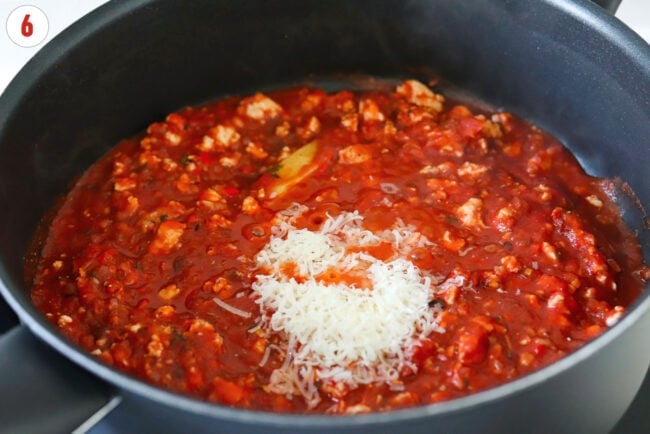 Fresh grated Parmigiano Reggiano cheese in a pan with tomato sauce and ground chicken.