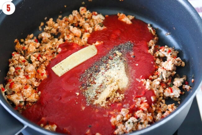 Parmigiano Reggiano cheese rind, seasonings, and passata in a skillet with sautéed ground chicken and aromatics.