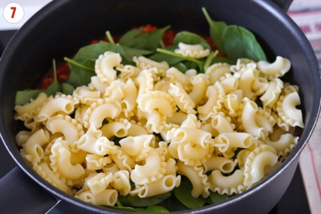 Cooked pasta and spinach in a skillet on the stove.