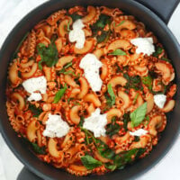 Pan with tomato basil pasta with spinach topped with basil and black pepper seasoned torn burrata.