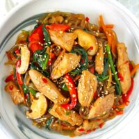 Korean japchae with chicken, carrots, mushrooms, spinach and bell pepper on a plate.